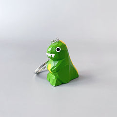 Close-up of a hand-painted dinosaur keychain with white teeth and big eyes, standing upright against a plain background.