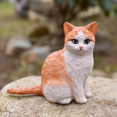 Custom cat figurine of a white and orange cat sitting on a rock, with finely painted eyes and carved fur details.