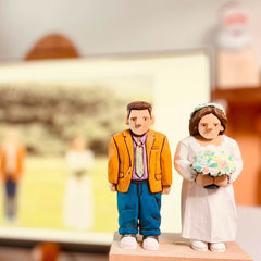 Hand-carved custom figurine of a couple in wedding attire, displayed with their wedding photo in the background.