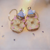 Two hedgehog keychains with pastel-painted details and tiny party hats, placed together on a soft, illuminated surface.