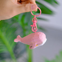 Pink whale keychain held up against a green background, highlighting its pink spray paint and speckled embellishments.