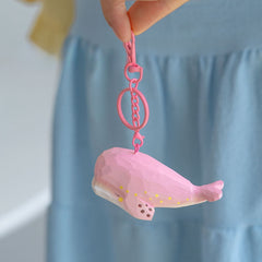 Pink whale keychain held against a blue dress, showcasing its charming and unique design.
