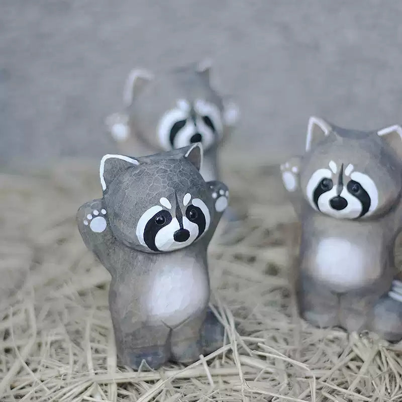 Three raccoon figurines together on dry grass