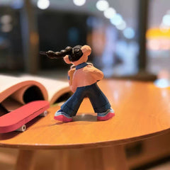Wooden skateboarder figurine back view showing long braid and red skateboard