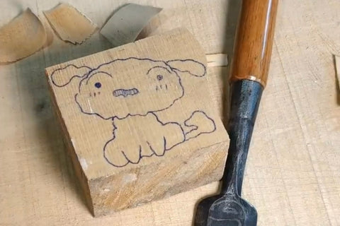 Shiro’s scalloped outline drawn on a wood block beside a carving tool