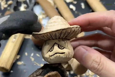 Finished mushroom wood carving with a textured cap and woodburned face held by hand