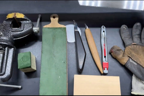 Carving knives, a leather strop, a small vise, gloves, and a wood block on a workbench