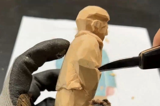 Close‑up of carving a wooden figurine, showing the knife shaping the sleeve and clothing folds — a detailed wood carving figures process for creating handcrafted wooden gifts.