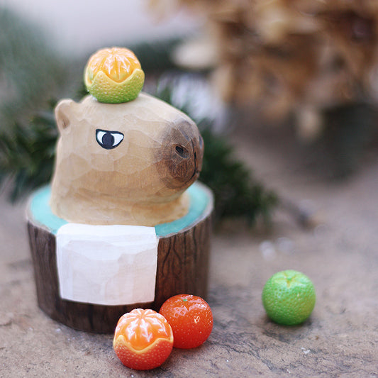 Bathing capybara sculpture in a bark-textured wooden tub with a white towel and small citrus pieces