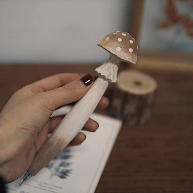Hand holding a brown mushroom pen with a white-spotted cap and angular carved stem.