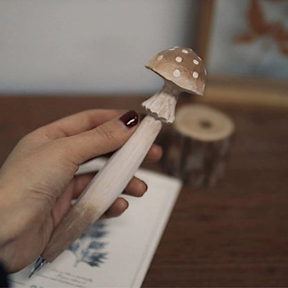 Hand holding a brown mushroom pen with a white-spotted cap and angular carved stem.
