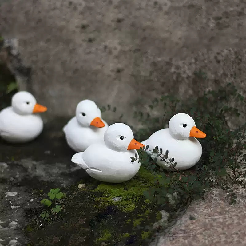 Four white Call Duck figurines arranged together on moss and stone