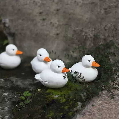 Four white Call Duck figurines arranged together on moss and stone