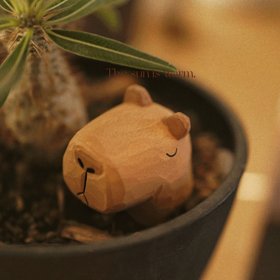 Wooden capybara figurine nestled beside a plant in a dark flowerpot
