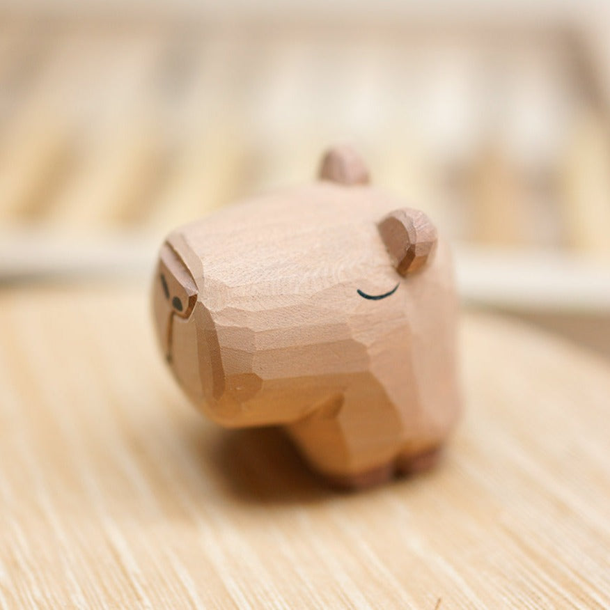 Side view of a wooden capybara figurine showing its closed eyes, broad muzzle and short legs