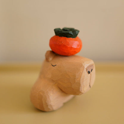Wooden capybara figurine with closed eyes and a persimmon balanced on its head