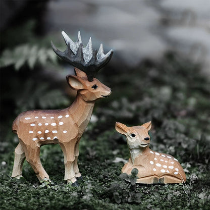 Two Christmas deer figurines, an antlered male standing beside a resting fawn on moss