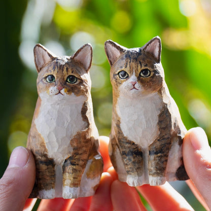 A pair of matching custom cat figurines held in hands, featuring brown and white tabby cats with expressive faces.