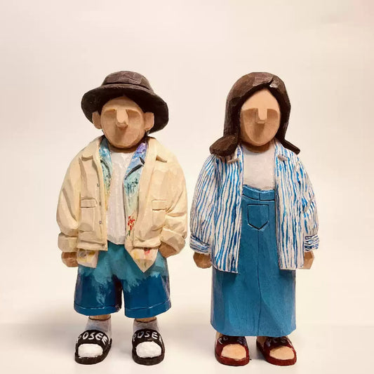 Two custom wooden couple figurines in casual outfits, one in a cream jacket and hat and the other in a striped shirt and blue skirt.