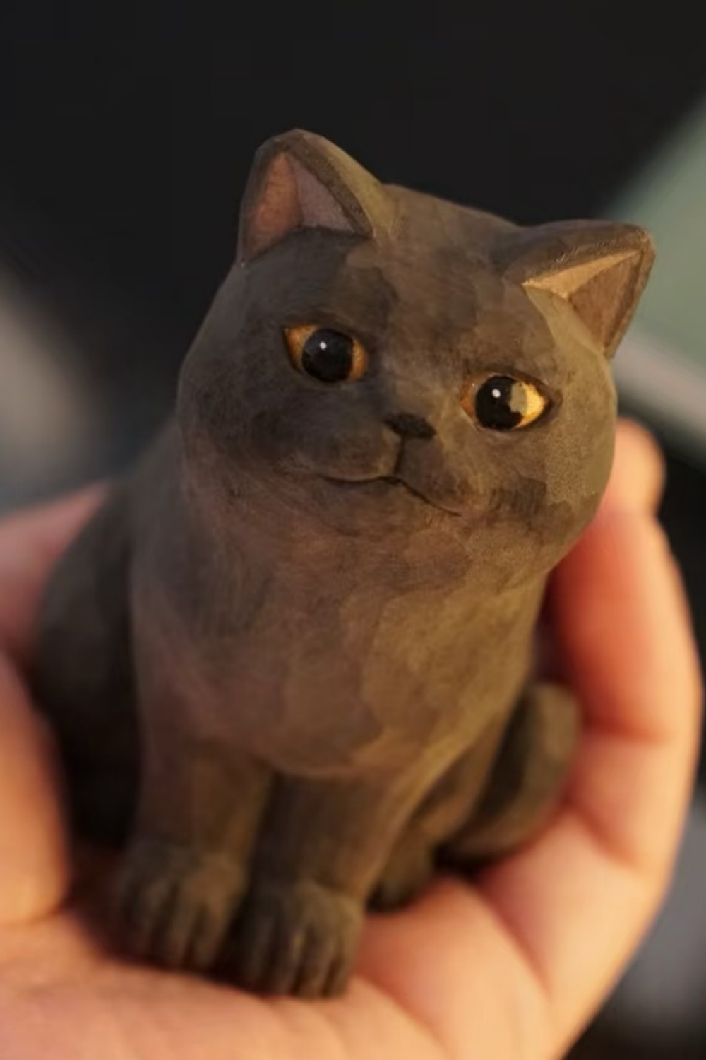 Hand-carved wooden British Shorthair cat figurine with round golden eyes and front paws together.
