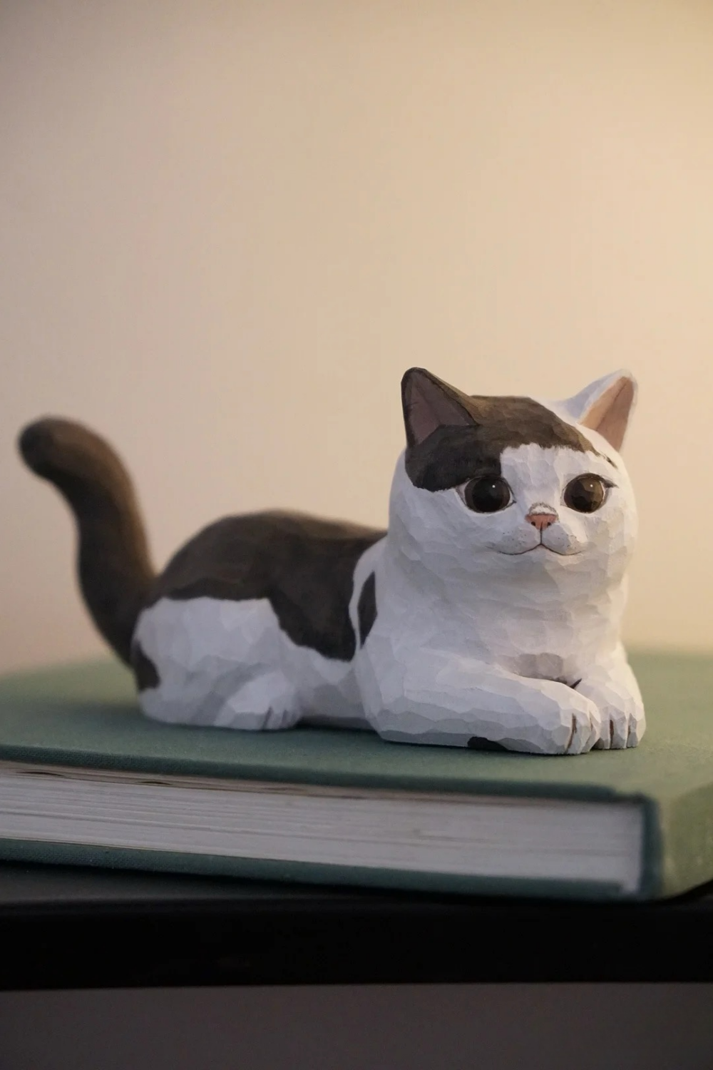 Hand-carved wooden bicolor cat figurine lying with its front paws extended and tail raised.