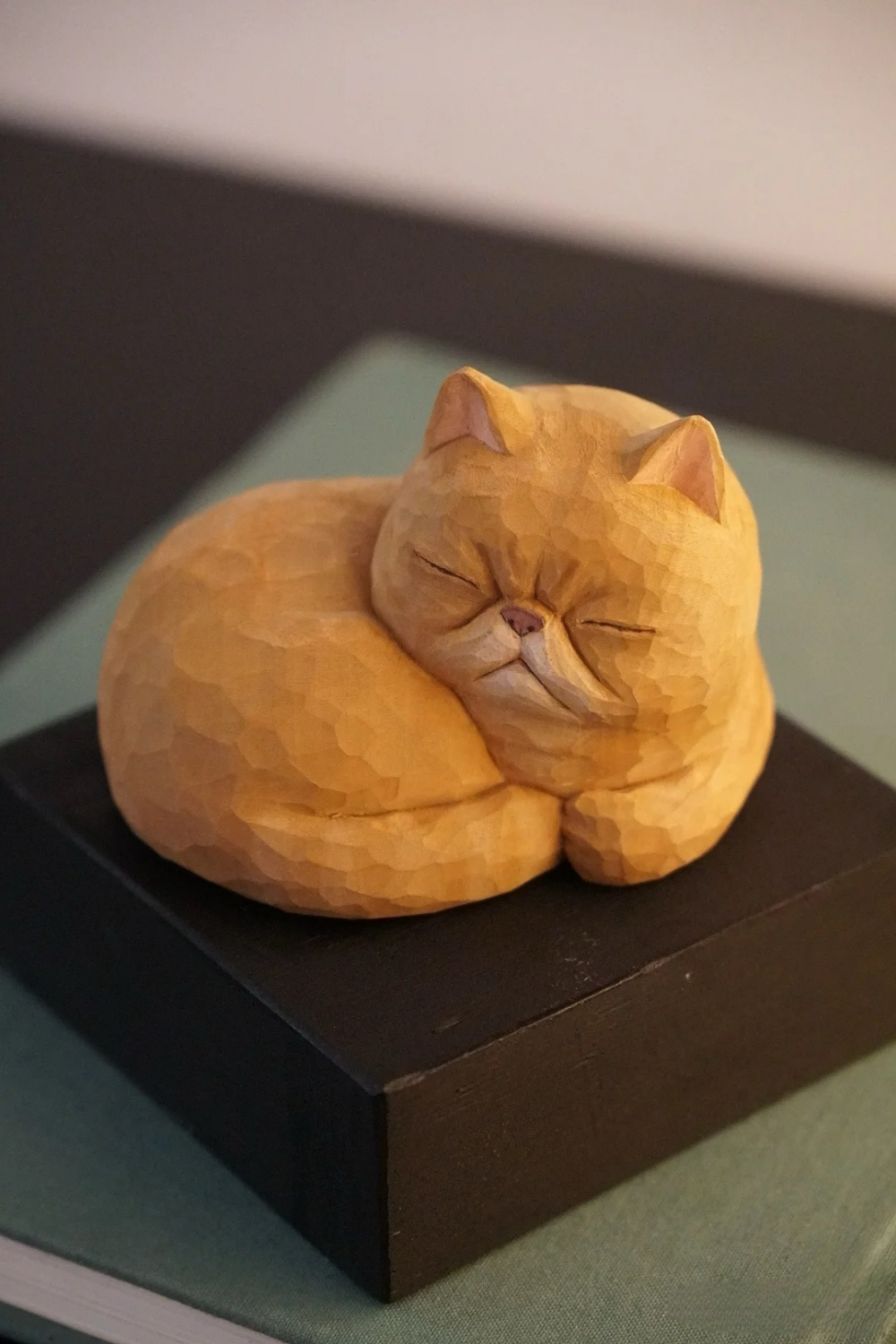 Hand-carved wooden ginger cat figurine curled up asleep with closed eyes and a tucked tail.
