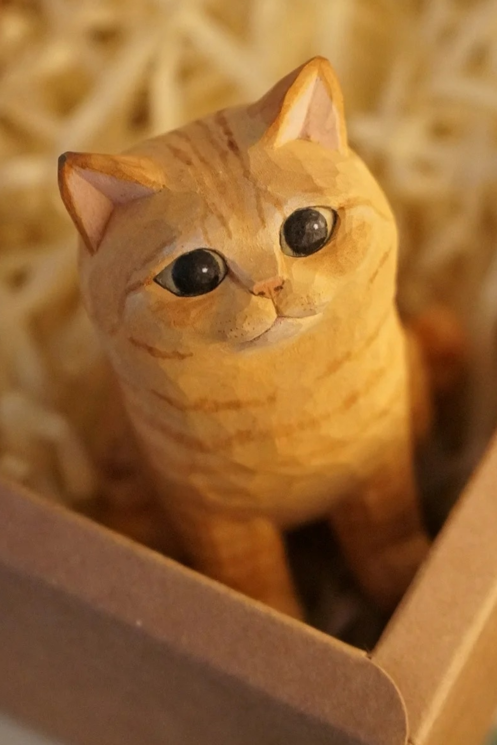 Hand-carved wooden orange tabby cat figurine with large round pupils and subtle painted stripes.