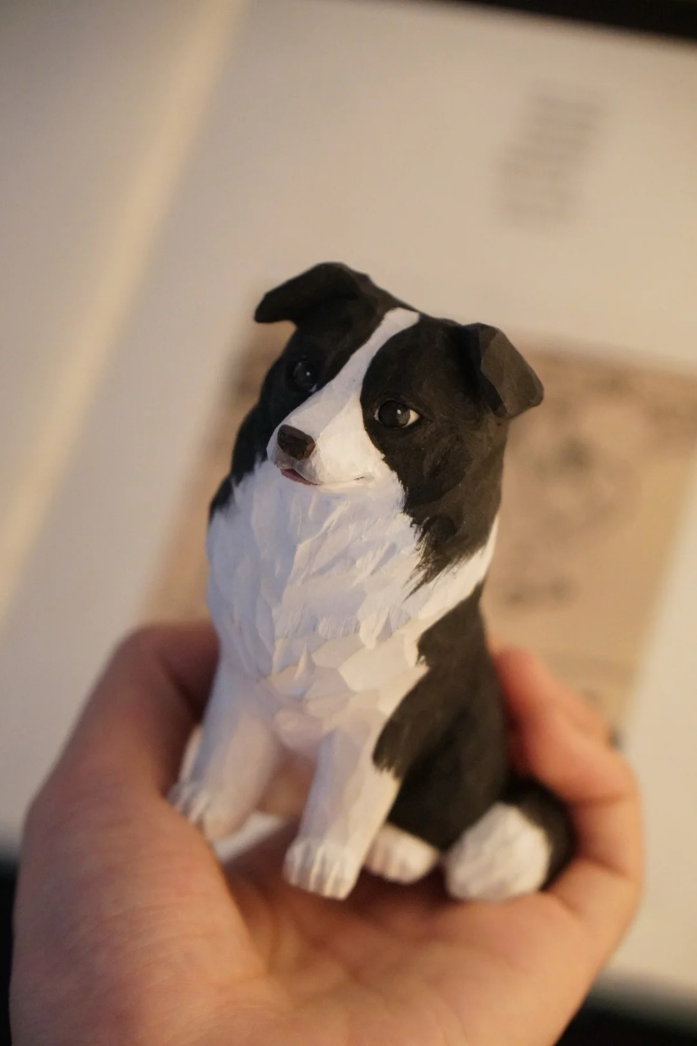 Hand-carved wooden Border Collie figurine with black-and-white markings, folded ears, and a seated pose.