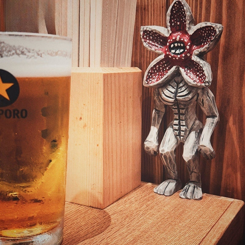 Wooden Demogorgon figure placed beside a beer glass in a cozy wooden interior.