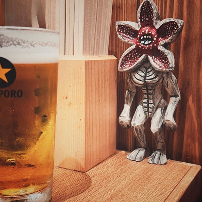 Wooden Demogorgon figure placed beside a beer glass in a cozy wooden interior.