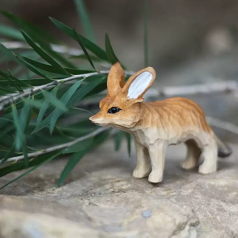 Fennec fox wooden figurine on rock with green foliage