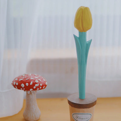 Yellow wooden tulip pen standing in its pot holder beside a red mushroom ornament.