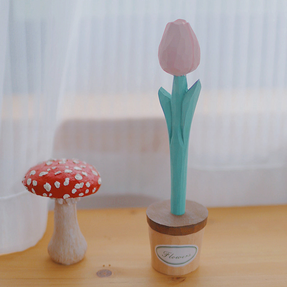 Light pink wooden flower pen standing in its pot holder beside a red mushroom ornament.