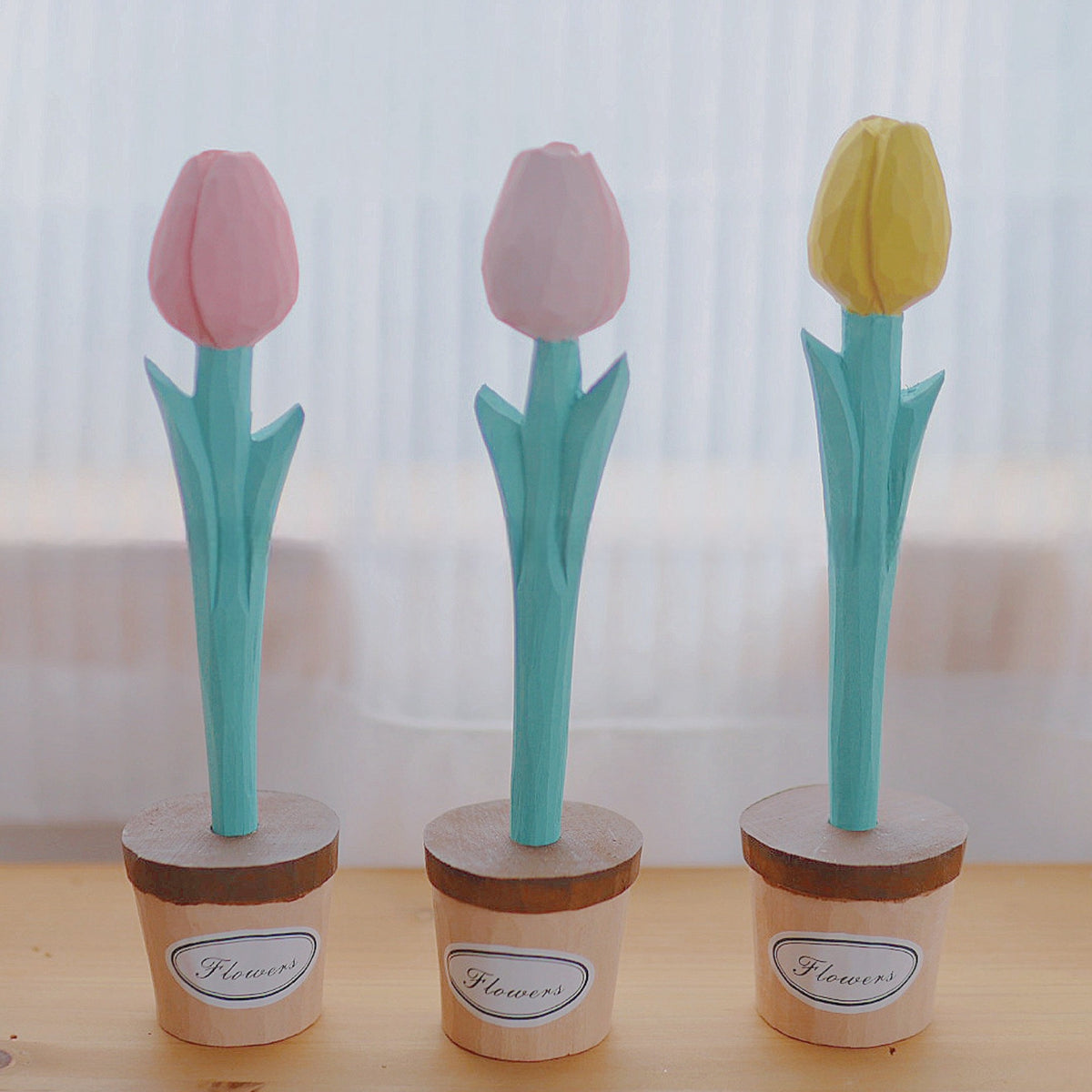 Three wooden tulip pens with pink and yellow blooms standing in individual wooden pot holders.