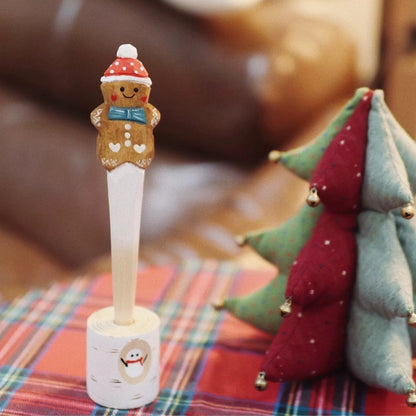 Wooden gingerbread pen standing in its snowman-painted holder beside a fabric Christmas tree
