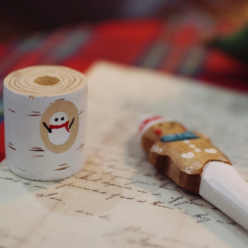 Snowman-painted wooden pen holder beside the gingerbread pen resting on handwritten paper