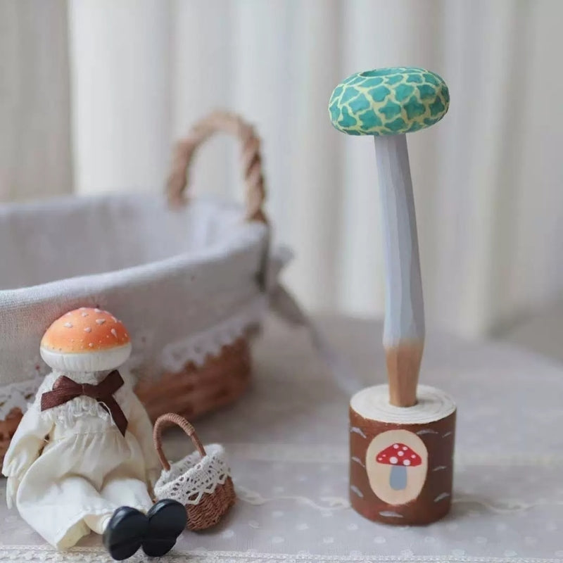 Green mushroom pen in a wooden holder beside a seated mushroom figurine with a small basket.