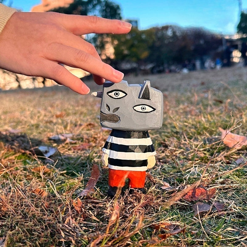 Small hand-carved Guernica-inspired figure placed on grass with a hand reaching towards it.