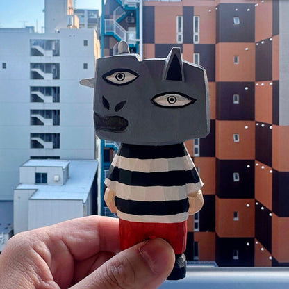 Hand holding abstract wooden monster figure with urban apartment buildings in the background.