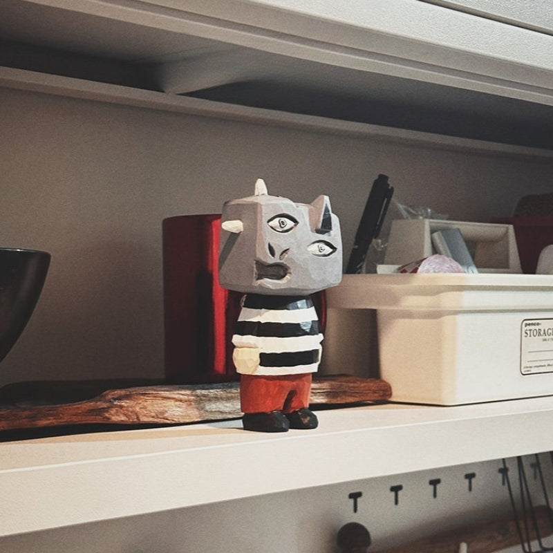 Wooden abstract monster figure displayed on a shelf among everyday household items.