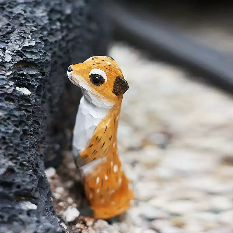 Hand-carved meerkat wooden figurine in rocky crevice