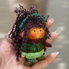 Close-up of handcrafted wood doll keychain with green scarf, soft yarn hair and hand-painted face