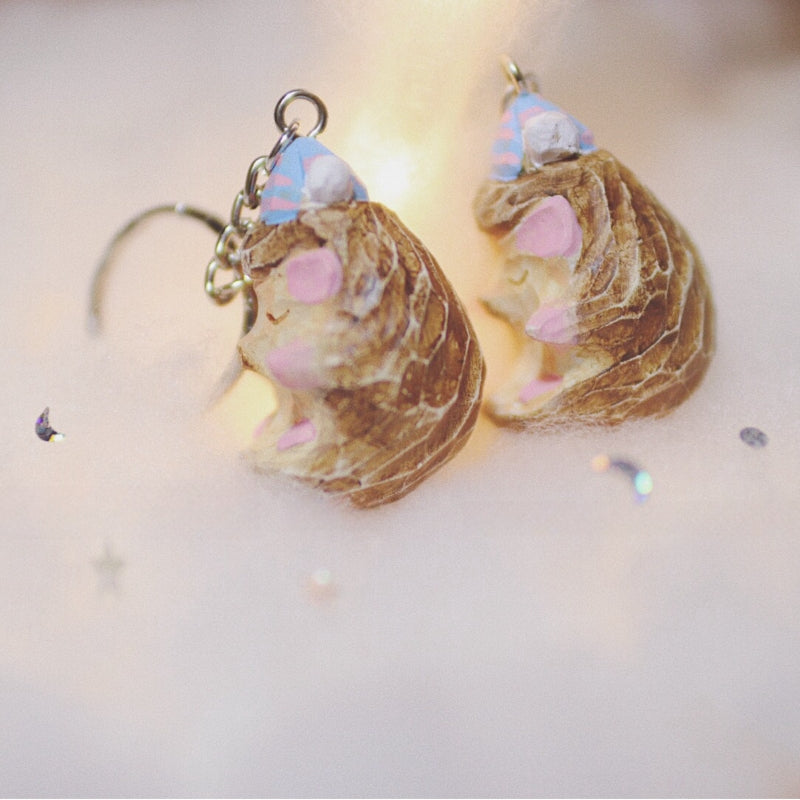 Back view of two hedgehog keychains with pastel-painted details and tiny party hats, highlighting the textured wood and artistic design.