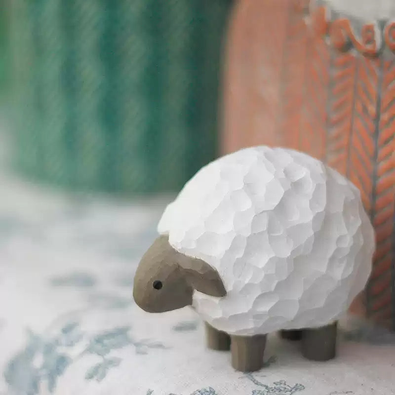 Lamb wooden figurine beside green ceramic pot on patterned cloth