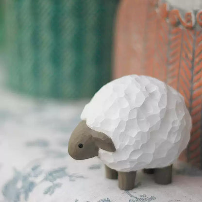 Lamb wooden figurine beside green ceramic pot on patterned cloth