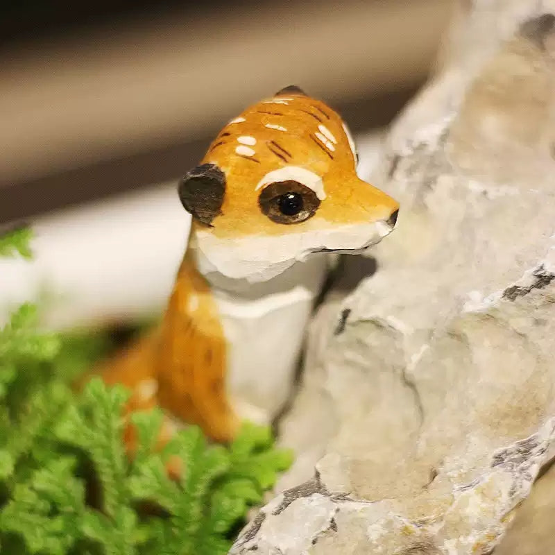 Close-up of meerkat figurine peeking around stone