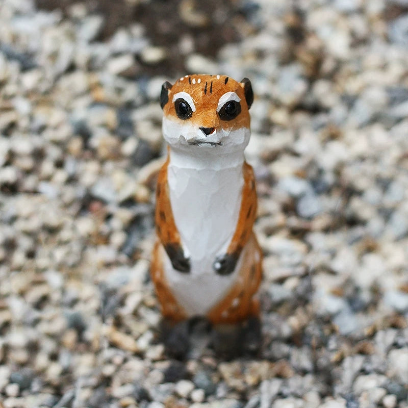 Front view of meerkat wooden figurine in sentinel pose on gravel