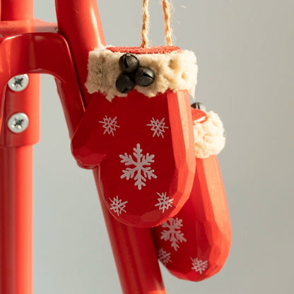 Black bells and fluffy tan cuffs on two red wooden mittens, with one hanging behind the other