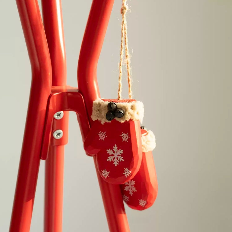 Pair of red wooden mitten ornaments hanging from twine against a red metal frame