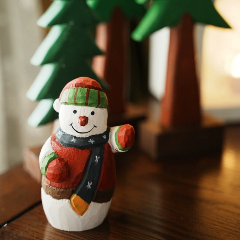 Painted snowman with a red vest and navy scarf standing in front of wooden Christmas trees
